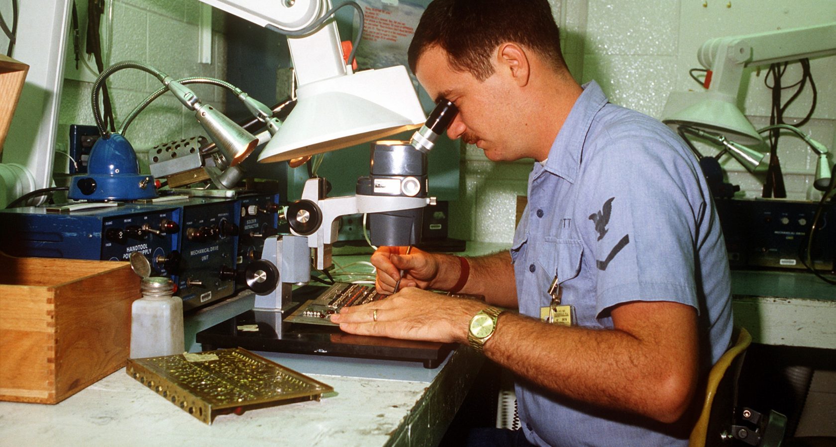 Technician performing detailed inspection work on a printed circuit board under a magnifier